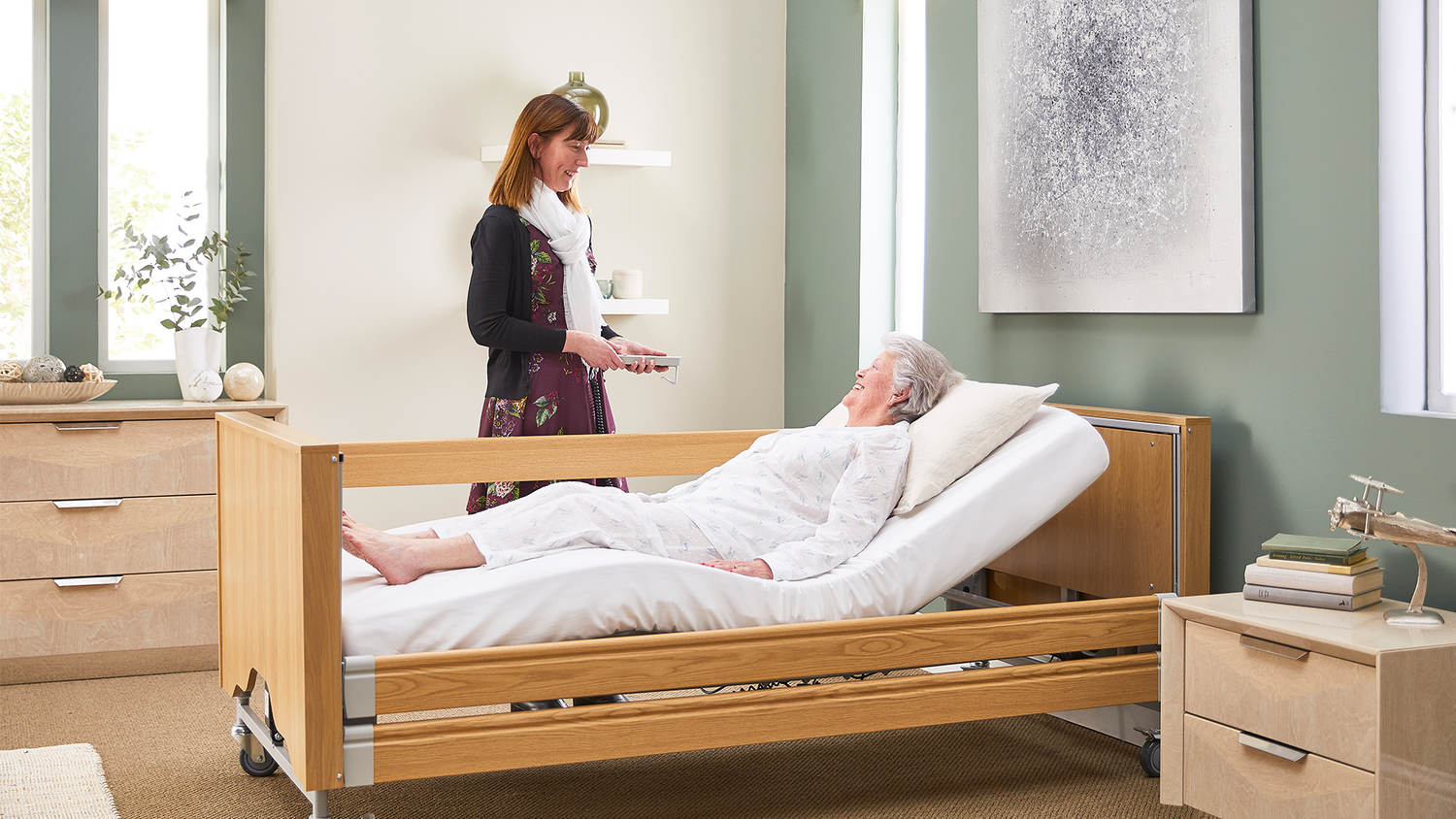 A female carer using a remote control to adjust a female patient in a profiling bed