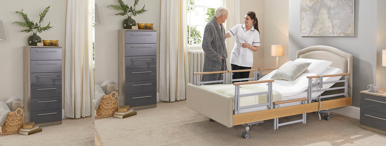 Man in a dressing own standing with a carer next to an Opera profiling bed with side rails