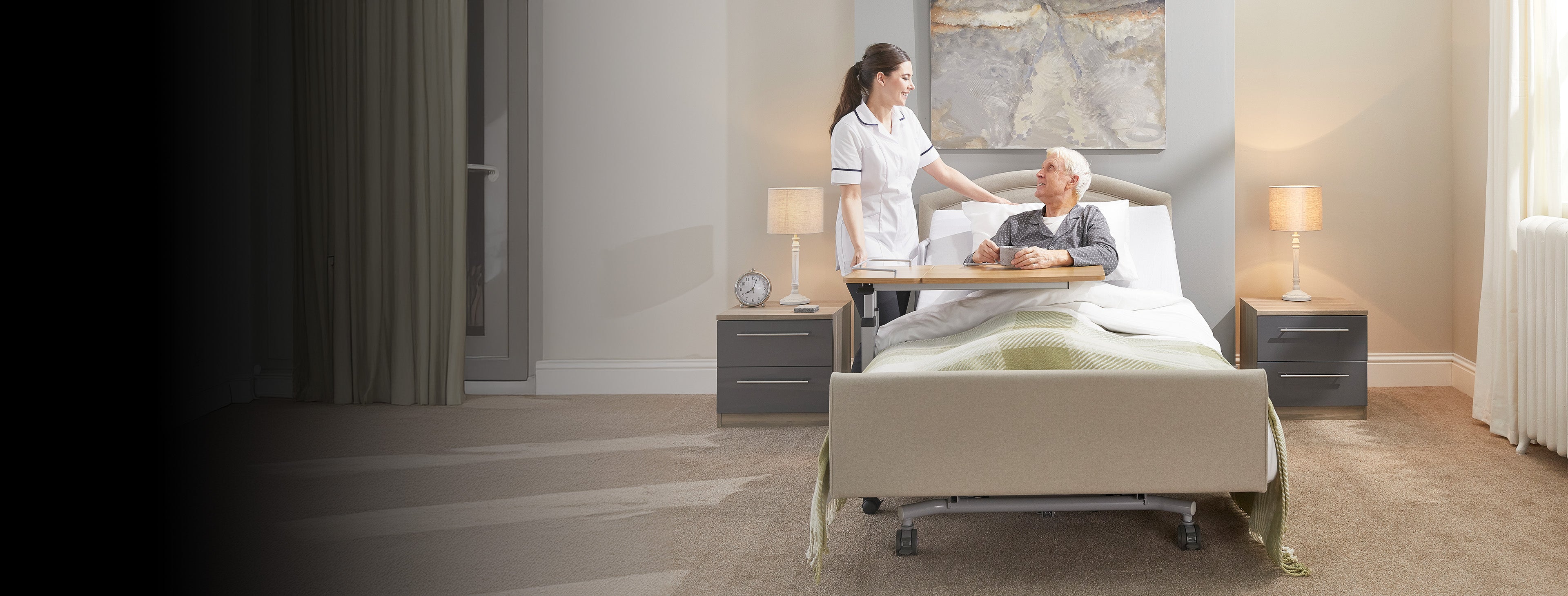 Person in a hospital bed with a nurse standing beside them in a room.